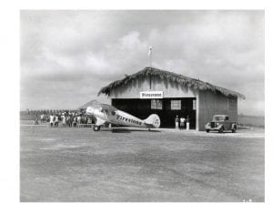 Airplane with the Firestone logo in front of a hangar and a group of people